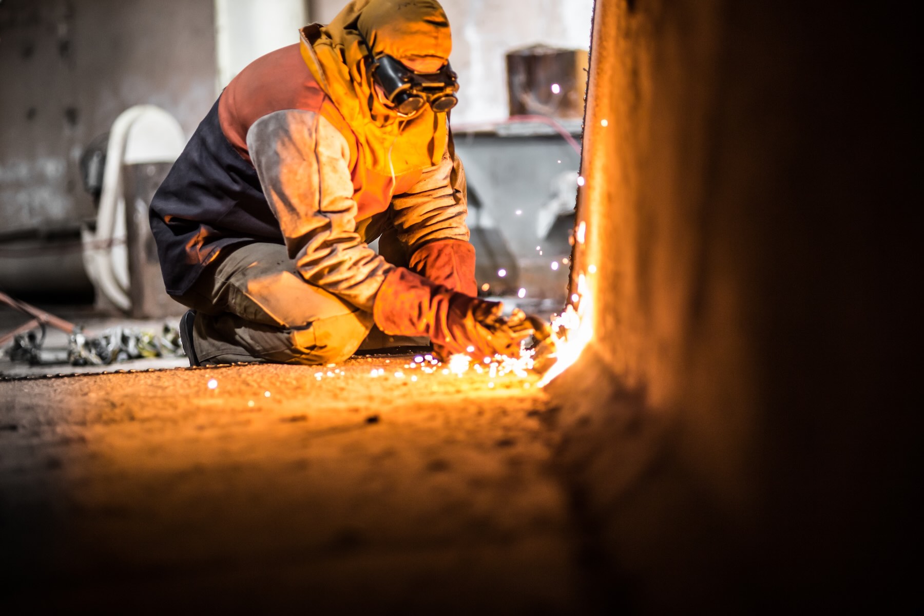 A demolition construction worker with full protective gear using a flame torch to cut up heavy machinery